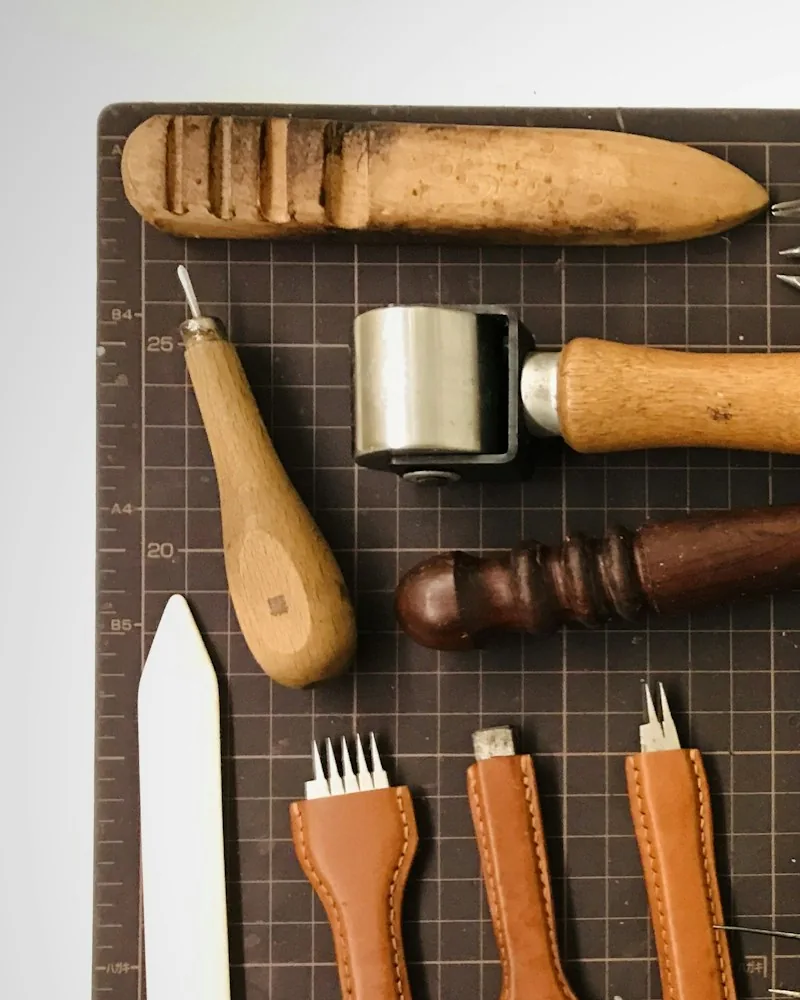 Herramientas de marroquinería y zapatería ordenadas sobre una base de corte: alisador de hueso, ruleta, punzón y matrices de puntear